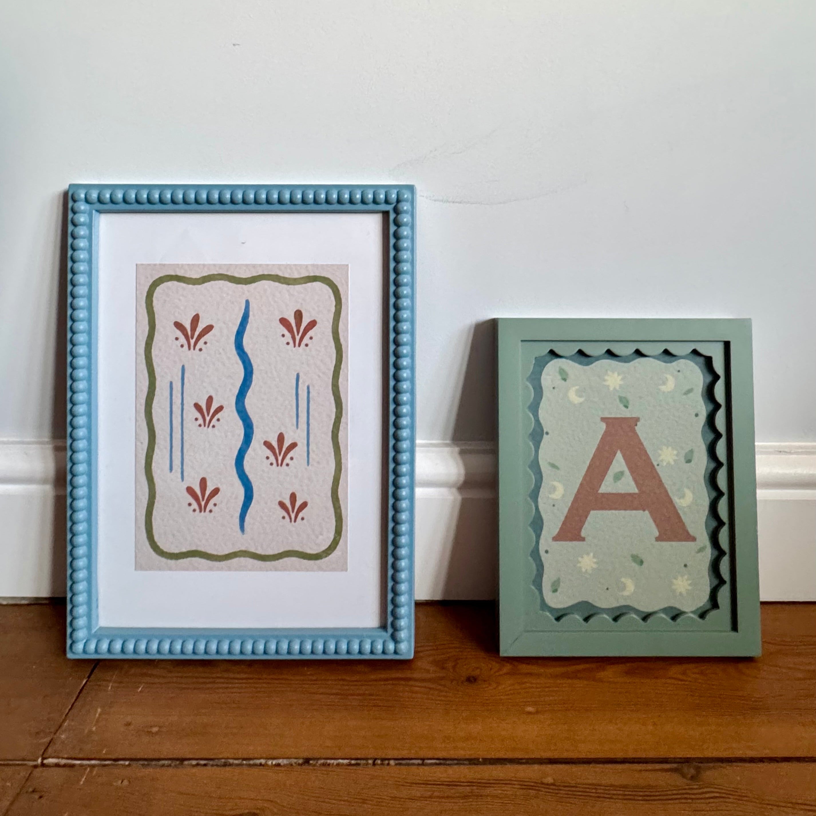 Two framed artworks on a wooden floor against a white wall